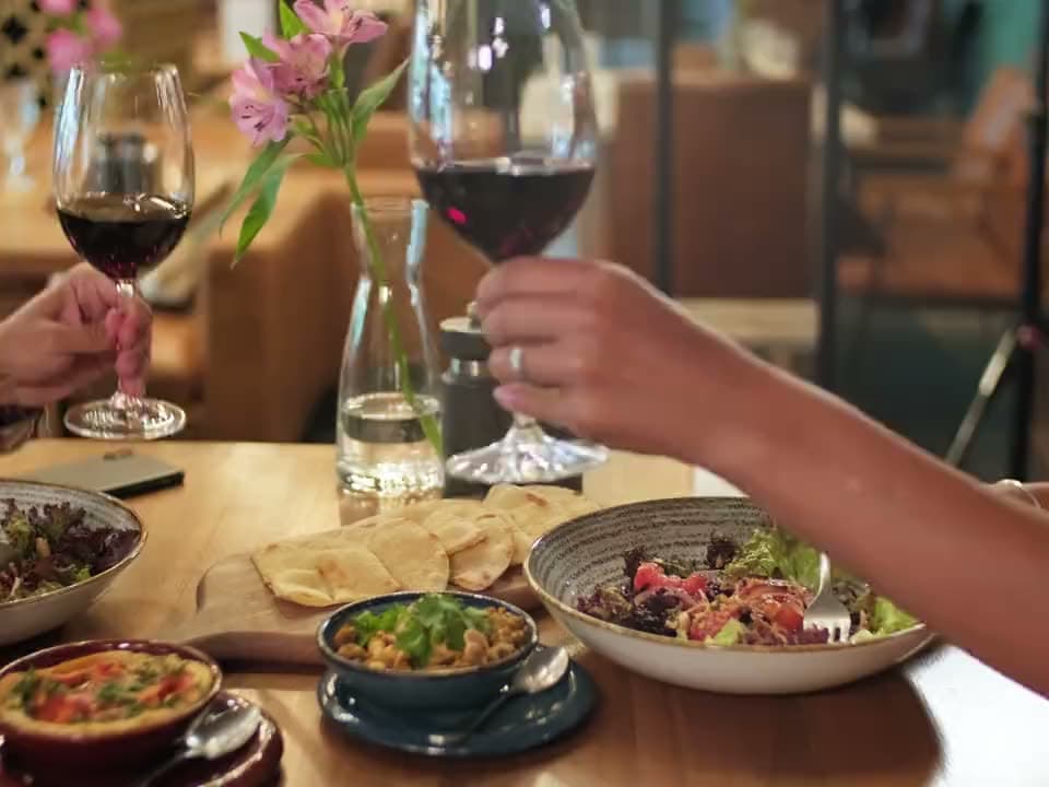 Twee mensen aan een gedekte tafel met gerechten en een glas wijn in een restaurant